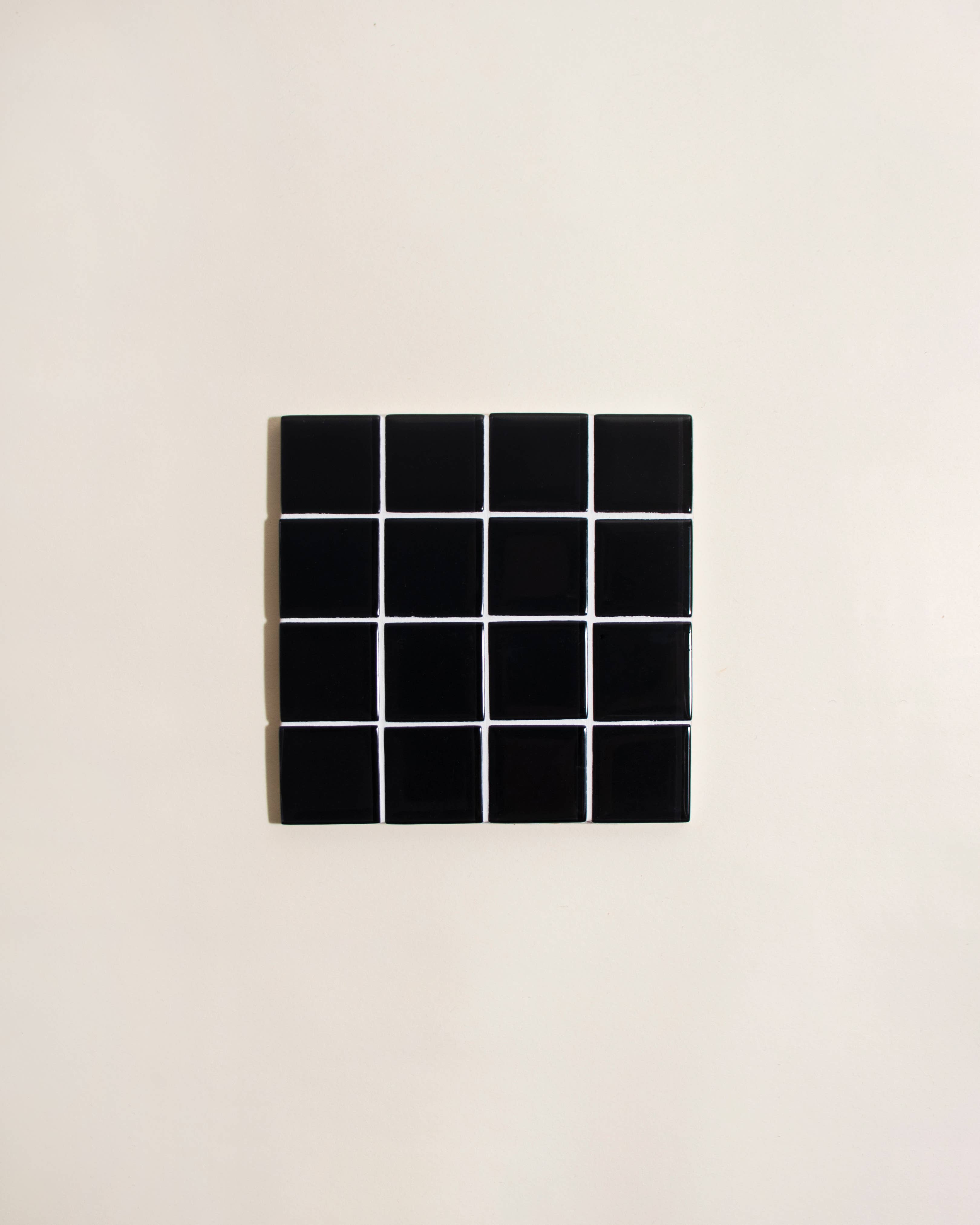 Black square tile with grid pattern on a beige background